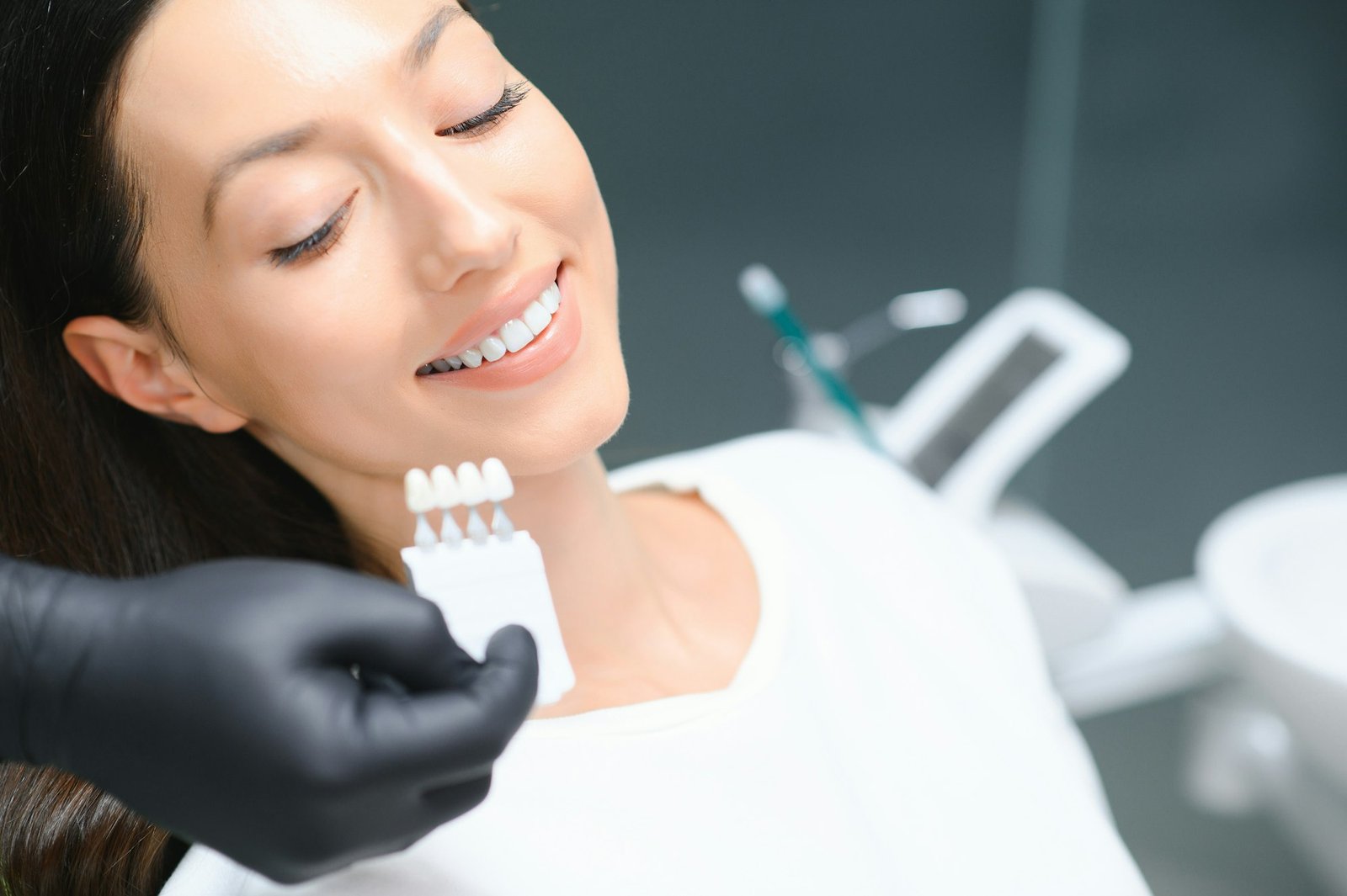 Dentist checking and selecting color of young woman's teeth