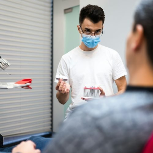 Dental surgeon with dental crown in hands model talks to patient about prosthetics.